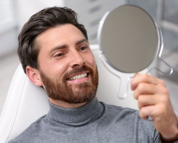 Man looking at his new dental implants in mirror indoors