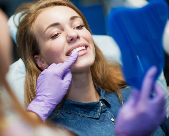 Dentist and a happy woman after chipped tooth repair looking at her teeth in a mirror.