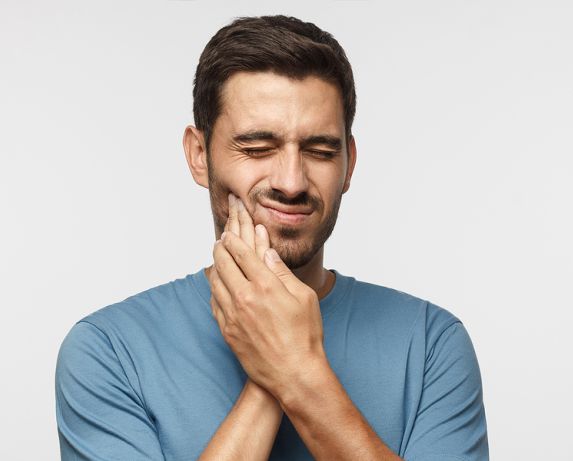 A man suffering from jaw pain due to TMJ syndrome touching his jaw