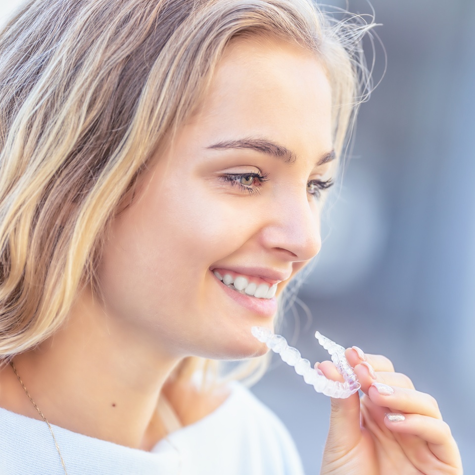 Invisalign orthodontics concept - Young attractive woman holding - using invisible braces or trainer.