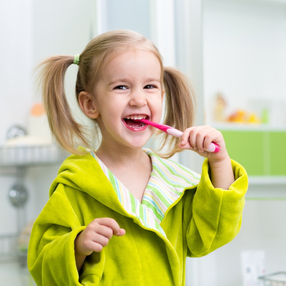 Smiling child kid girl brushing teeth in bathroom