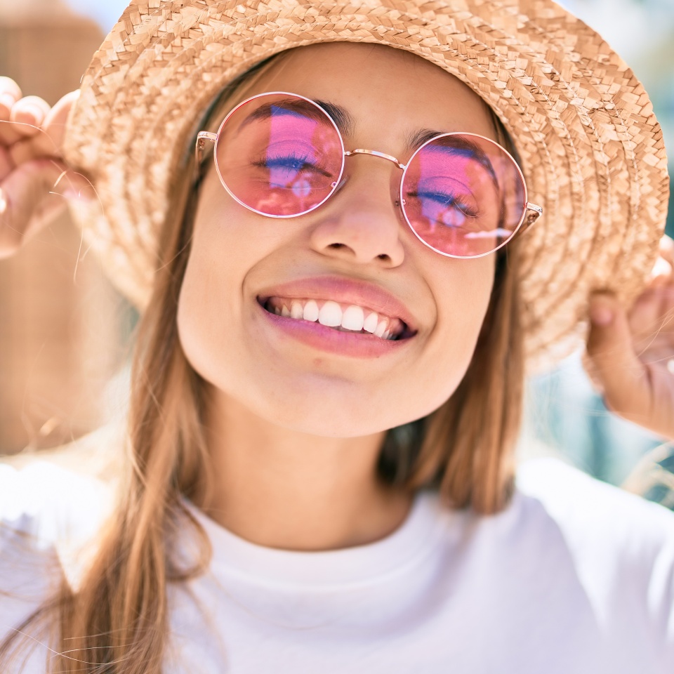 Young beautiful blonde caucasian woman smiling happy outdoors on a sunny day wearing summer hat and pink sunglasses