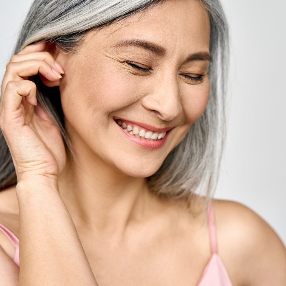 Portrait of gorgeous happy middle aged mature cheerful asian woman, senior older 50s lady pampering her face eyes closed isolated on white. Ads of lifting anti wrinkle skin care, spa. Copy space.