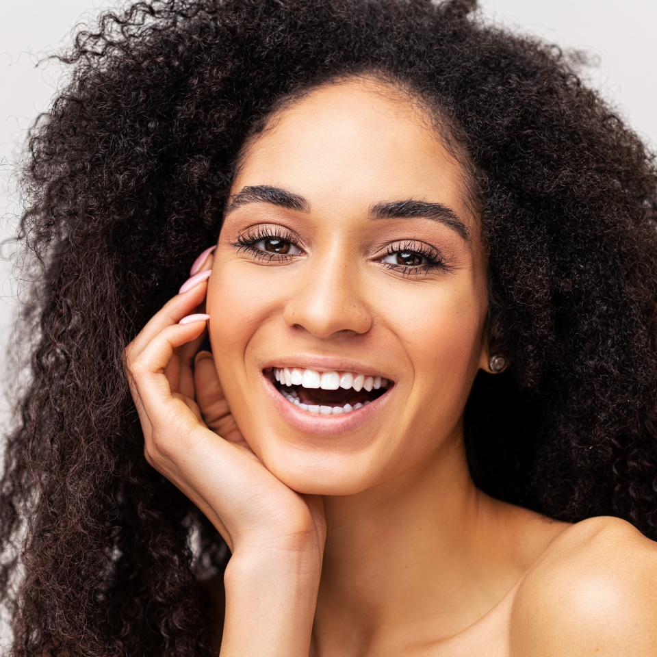 Magnificent african-american woman isolated on white background looking at the camera and smiling toothy. Well-looking young multiracial lady with naked shoulders laughing playfully. Selfcare concept