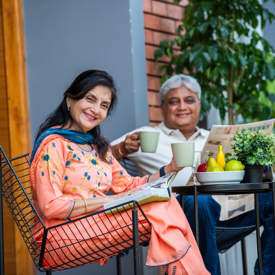 Elderly Indian asian couple reading newspaper and book while listning to music and having breakfast outdoors in gallery