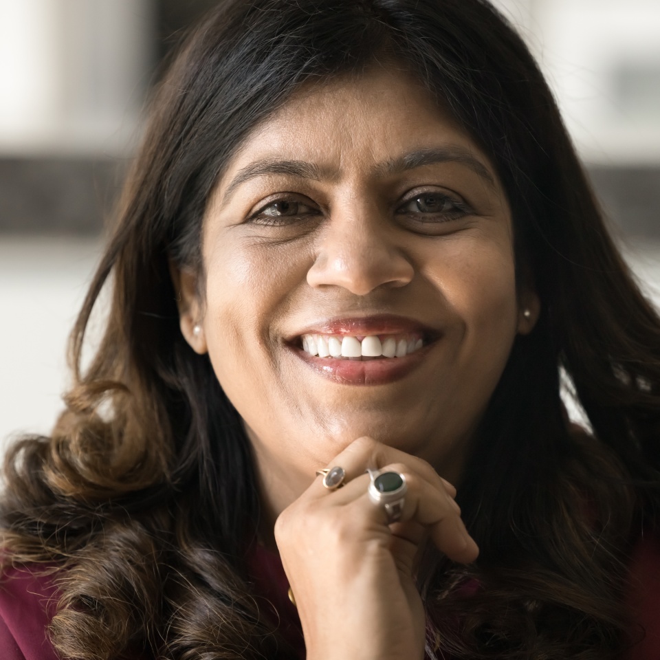 Close facial portrait of happy mature Indian woman with wavy black hair looking at camera, smiling, showing healthy white teeth, touching face, chin, promoting dental care. Cropped head shot, closeup