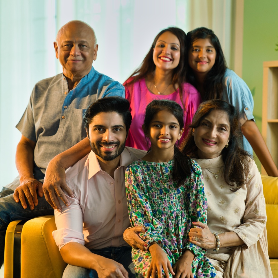 Closeup of Indian Asian multigenerational family of six sitting together on a sofa in a luxurious home, sharing happy moments and bonding across generations