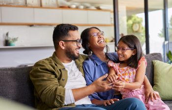 Cheerful middle eastern family with eyeglasses of three having fun together at home. Mixed race parents talking with their little girl in living room. Cheerful family with specs embracing and playing.