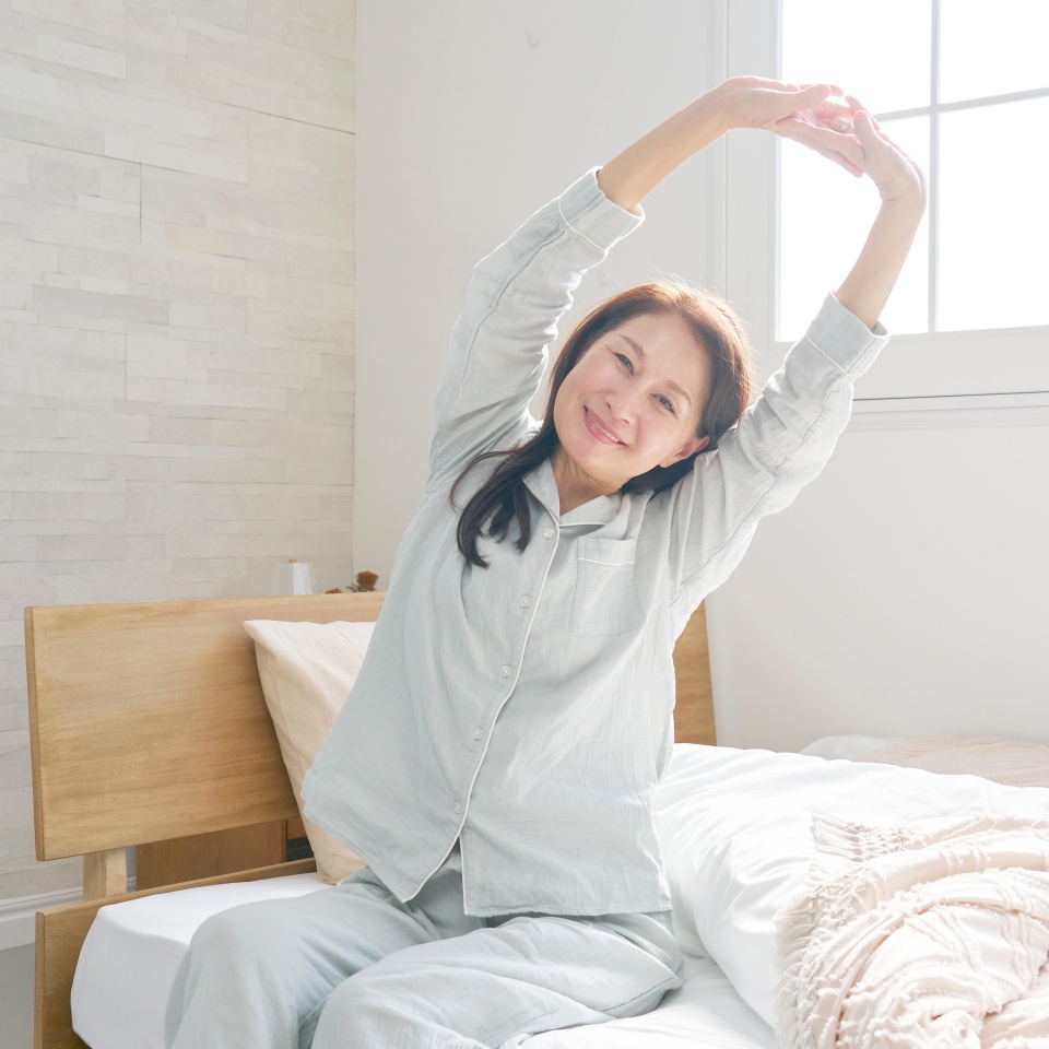 Asian 60s woman in the pajamas stretching the body in the room