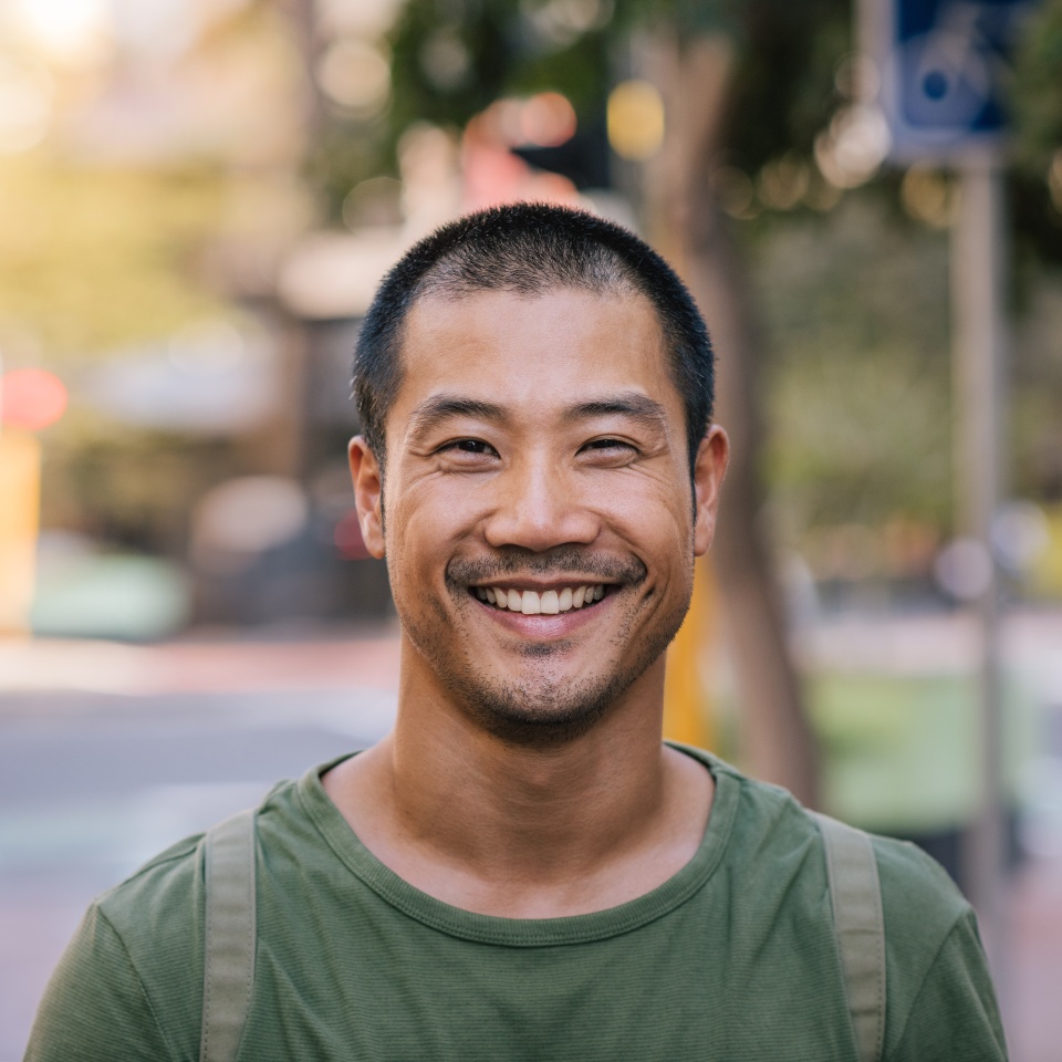 Portrait of a casually dressed handsome young Asian man smiling while standing alone outside on a city street on a sunny day