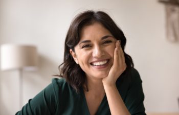 Beauty and wellness. Head shot portrait beautiful young adult woman with light natural makeup on face sit indoors in comfortable pose look at camera with white smile enjoy healthy lifestyle self care