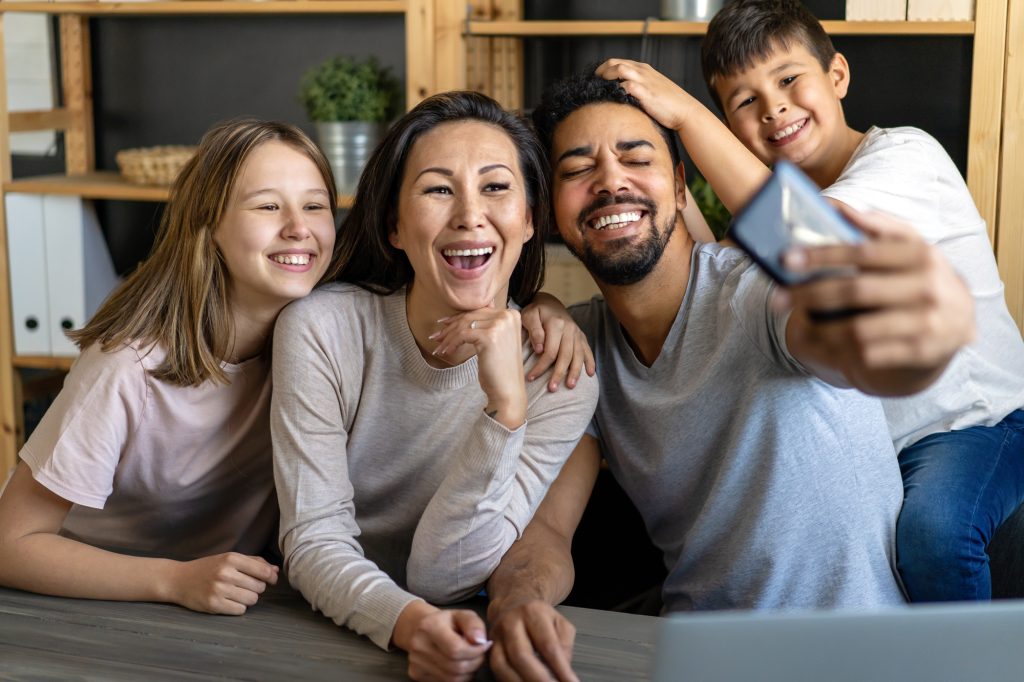 A family of four smiles and poses together for a selfie in a home office setting.