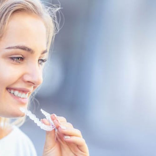 Invisalign orthodontics concept - Young attractive woman holding - using invisible braces or trainer.