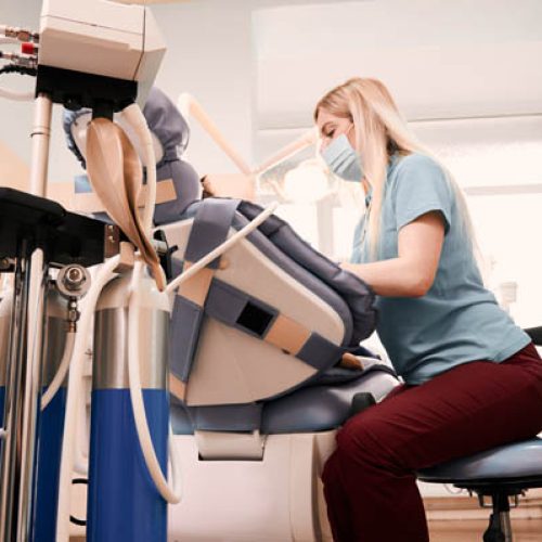 Side view of dentist treating kid teeth while child lying in dental chair. Equipment of inhalation sedation on foreground. Concept of children dentistry, stomatology and dental care.